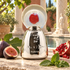 Agatho Parfum 195 a.C. bottle with figs, pomegranate, and mint in a sunlit Roman-inspired courtyard.