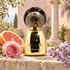 Agatho Parfum Adone beside pink grapefruit, a pink rose, and lavender wisteria on limestone in a sunlit classical courtyard.