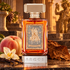 Argos Triumph of Bacchus perfume beside a whole peach, vanilla orchid and tobacco leaf in a warmly lit classical setting.