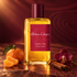 Atelier Cologne Ambre Nue on reddish stone with mandarin, cinnamon bark, and a burgundy orchid in warm golden light.