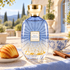 Atelier des Ors Blue Madeleine on a sunlit villa terrace with a madeleine, steaming black tea, cinnamon sticks, and pale blue linen.