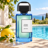 BDK Parfums Citrus Riviera bottle beside lemon and white blossoms on sunlit stone, with a turquoise pool and softly blurred Riviera coastline behind it.