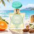 BillyXClub Conga Beatz bottle on sunlit wood beside a mandarin half, tamarind pods, and white blossoms, with turquoise waves and a conga drum behind.