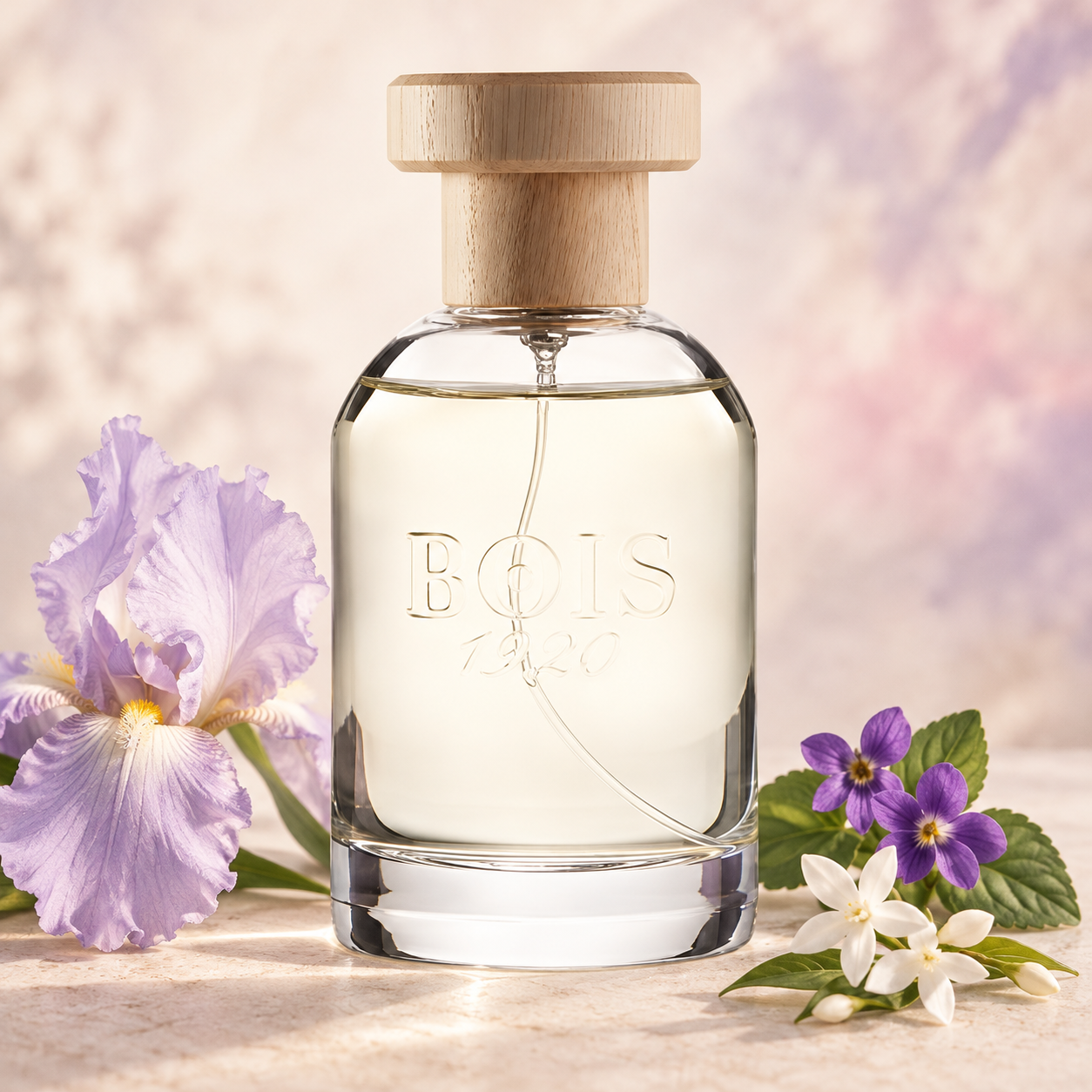 Bois 1920 Ancora Amore on pale stone beside a lilac iris, purple violets, and white jasmine against a softly lit pastel backdrop.
