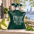 Bond No. 9 Beekman Place beside pear, basil, and driftwood on sunlit limestone, with townhouses and a river view behind it.