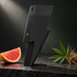 Carolina Herrera Bad Boy Le Parfum’s matte-black lightning-bolt bottle on dark stone beside grapefruit, hemp leaves, and vetiver roots.