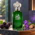 Clive Christian Contemporary’s emerald bottle on charcoal stone beside blackberries, violet blossoms, and nutmeg in soft directional light.