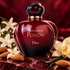 Dior Hypnotic Poison perfume on burgundy stone beside almonds, white blossoms, and vanilla pods in soft dramatic light.