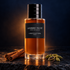 Dior Ambre Nuit Esprit de Parfum on dark stone with cinnamon quills and green cardamom pods, lit by an amber glow against a midnight-blue background.