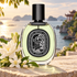 Diptyque Do Son EDP bottle with white tuberose and orange blossoms on coastal stone beside a softly blurred Vietnamese pagoda and sea.