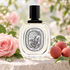 Diptyque Eau Rose EDT bottle with a pink rose and whole lychees on pale limestone in soft garden light.