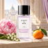 Eight & Bob Pure Vienne perfume on a sunlit windowsill beside pink peony, lily-of-the-valley, and a whole mandarin, with classical architecture beyond.