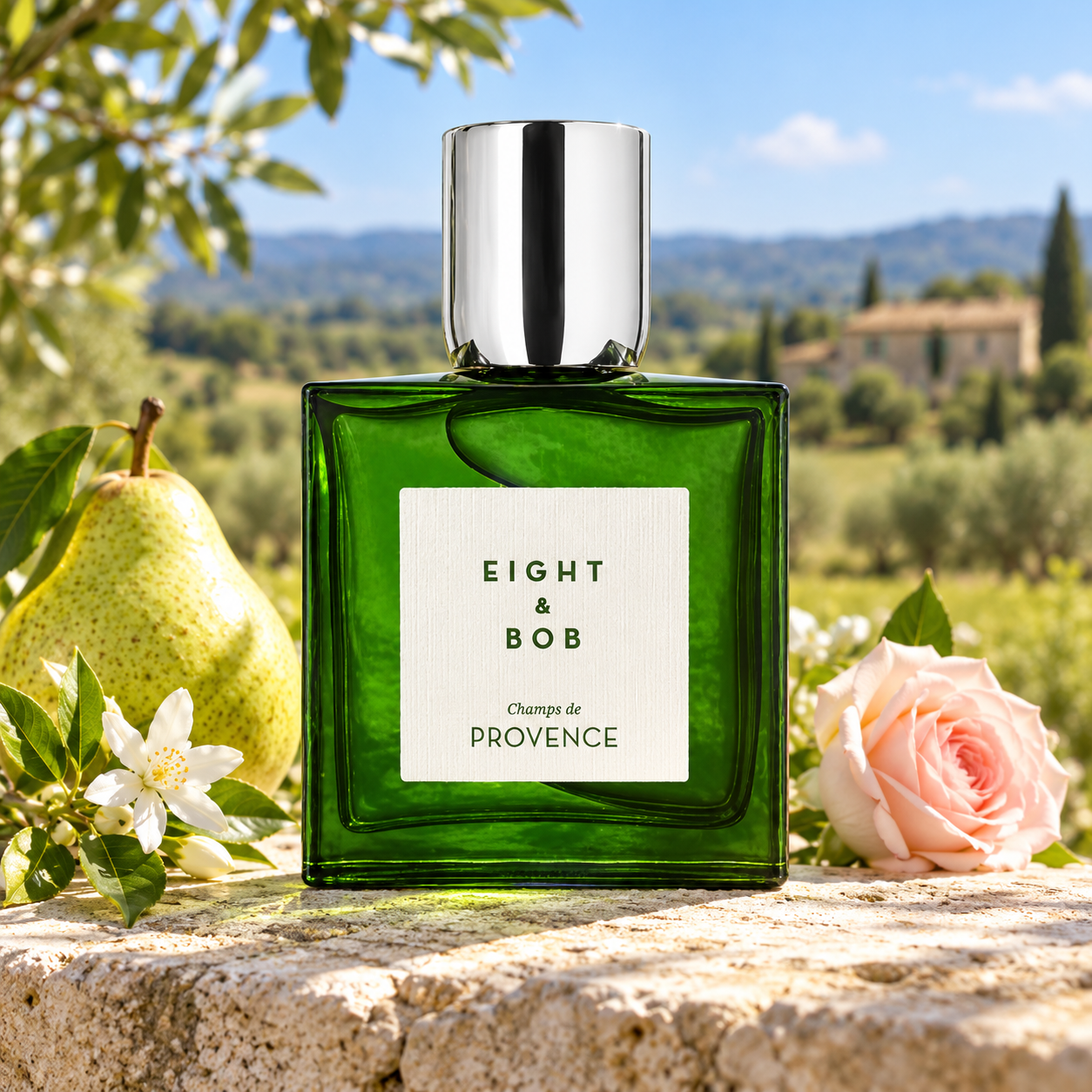 Eight & Bob Champs de Provence on sunlit limestone beside a pear, jasmine, and pink rose, overlooking green countryside and a stone farmhouse.