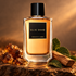 Elie Saab Essence No. 3 Ambre perfume on dark stone beside amber-colored resin, sandalwood, and green leaves in warm light.