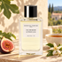 Essential Parfums Fig Infusion on a sunlit stone terrace with a cut fig, a cup of black tea and white orange blossoms.