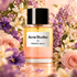 Acne Studios par Frédéric Malle stands amid orange blossoms, purple violets, and blush roses in warm peach light.