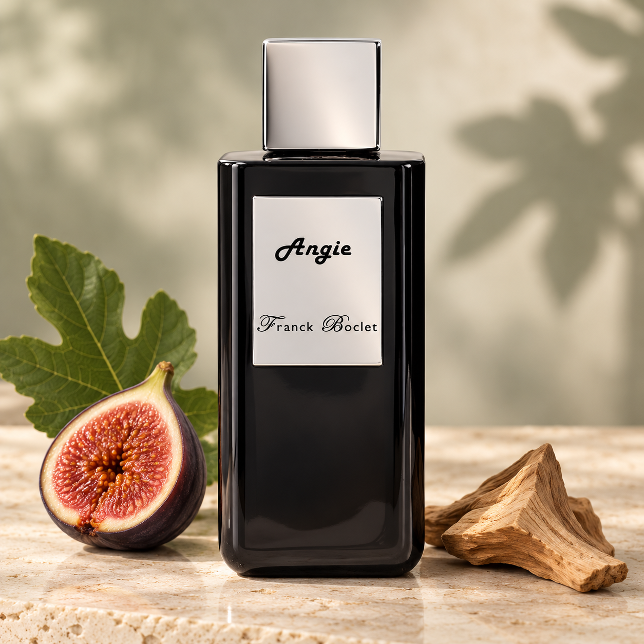 Franck Boclet Angie on ivory stone beside a halved fig, a green fig leaf, and pale sandalwood in soft warm light.
