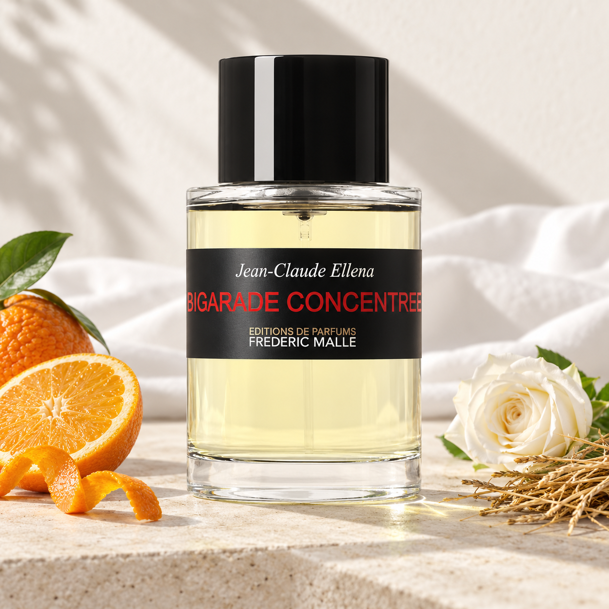 Frédéric Malle Bigarade Concentrée beside bitter orange, white rose, and hay on pale stone with white cotton and soft sunlight.
