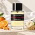 Frédéric Malle Bigarade Concentrée beside bitter orange, white rose, and hay on pale stone with white cotton and soft sunlight.