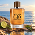 Giorgio Armani Acqua di Giò Absolu on wet driftwood beside bergamot, rosemary, and patchouli leaves, overlooking the sea in warm sunlight.