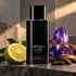 Armani Code Parfum’s black bottle on charcoal stone beside bergamot, purple iris, tonka beans, and wood under soft warm light.