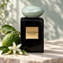 Armani Privé Eau de Jade black bottle with its pale jade cap beside bergamot and white neroli blossoms on softly lit limestone.