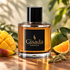 Gisada Ambassador Men stands beside mango, green mandarin, and cardamom on sunlit teak wood against a soft green backdrop.
