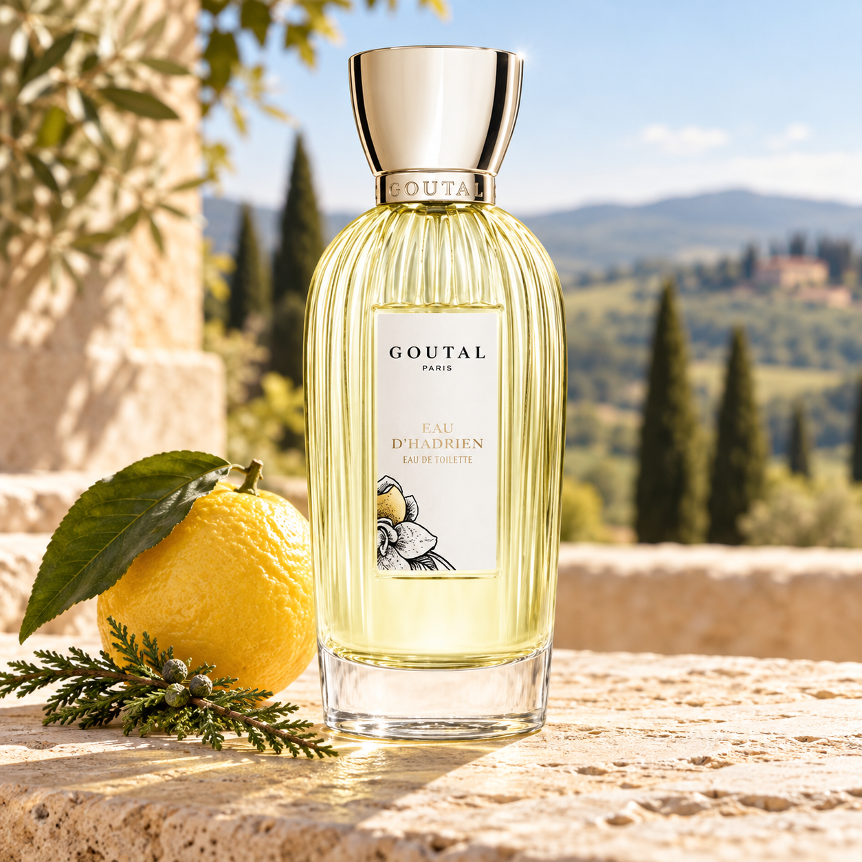 Goutal Eau d’Hadrien bottle with a whole lemon and cypress sprig on a sunlit stone terrace overlooking Tuscan hills.