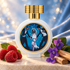 HFC Delicious Kisses perfume bottle framed by raspberries, purple violets, and sandalwood on ivory stone against softly shimmering blue fabric.
