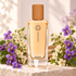 Hermès Cuir d’Ange perfume bottle framed by abundant purple violets and white hawthorn blossoms on ivory stone, with a subtle camel suede accent.