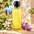 Hermès Eau de Néroli Doré yellow bottle with white neroli blossoms and purple saffron crocuses on sunlit Mediterranean stone.