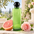 Hermès Eau de Pamplemousse Rose green bottle beside a pink grapefruit half and pale pink rose on sunlit terrace stone.