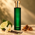 Emerald green Hermetica Amberbee bottle beside bergamot, a vanilla orchid, vanilla pods, and opoponax resin on pale stone in warm golden light.