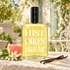 Histoires de Parfums 1873 with grapefruit, orange blossoms, and vanilla pods on a sunlit stone table in a French-style garden.