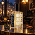 Histoires de Parfums 1899 bottle with juniper berries, cinnamon, and vanilla pods in a warmly lit Parisian café at night.