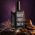 Histoires de Parfums Irrévérent on dark stone with lavender, oud wood and coffee beans against a softly lit plum backdrop.