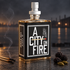 A City on Fire bottle beside burnt matches, blackberries, and cardamom against a softly blurred waterfront at dusk.