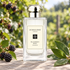 Jo Malone London Blackberry & Bay on weathered wood beside ripe blackberries and fresh bay leaves in a softly sunlit garden.