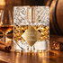 Kilian Angels’ Share on warm oak beside cinnamon, a praline chocolate, and a cognac glass, with an oak barrel softly blurred behind.