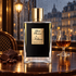 Kilian Black Phantom on a polished café table with dark chocolate, coffee beans, and a glass of rum beside a rain-streaked Parisian window.