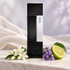 Laurent Mazzone Aldhèyx’s tall black bottle beside white jasmine, purple heliotrope, and bergamot on pale stone, with ivory fabric and soft lilac light behind it.