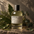 Le Labo LAURIER 62 home fragrance bottle surrounded by laurel leaves, rosemary, and eucalyptus on textured stone in warm directional light.