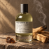 Le Labo PALO SANTO 14 home fragrance bottle beside palo santo wood and dark resin on textured stone, with curling smoke in warm golden light.
