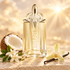 MUGLER Alien Goddess’s golden bottle stands beside coconut, white jasmine, a pale orchid, and vanilla pods in warm sunlight.
