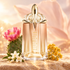 MUGLER Alien Goddess Supra Florale’s peach and gold bottle stands beside a pink cactus flower, white jasmine, and golden immortelle in warm sunlight.