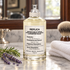 Maison Martin Margiela At the Barber’s on a marble counter beside lavender, rosemary, a folded white towel, and a shaving brush, with a vintage mirror behind it.