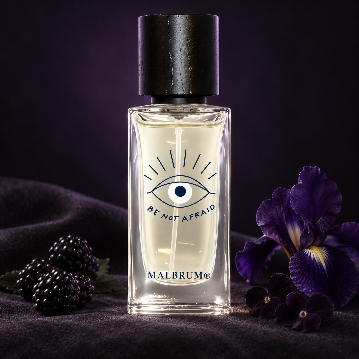 Malbrum Parfums Bagheera on dark suede beside blackberries, a deep purple iris, and near-black violets in soft violet light.
