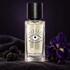 Malbrum Parfums Bagheera on dark suede beside blackberries, a deep purple iris, and near-black violets in soft violet light.