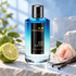 Mancera Aoud Blue Notes beside bergamot, a pale pink rose, and vanilla pods on pale stone in cool daylight.