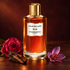 Mancera Aoud Exclusif beside a deep pink rose, saffron crocus, and oud wood on brown leather in warm amber light.